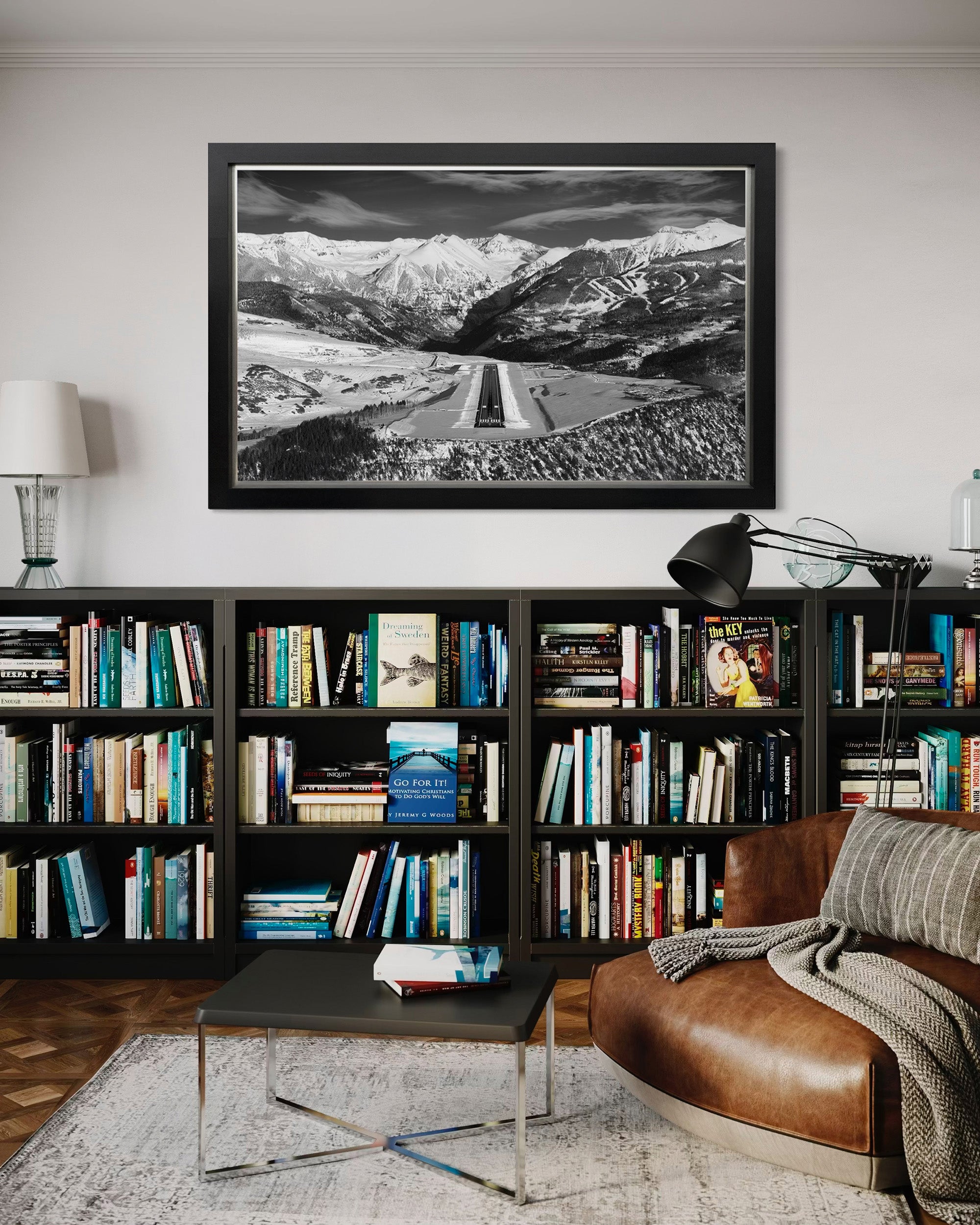 Living room with bookshelf, sofa, and framed black and white mountain landscape